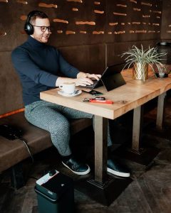 Mann arbeitet an seinem Computer im Café, während die Batterie des Rollers geladen wird